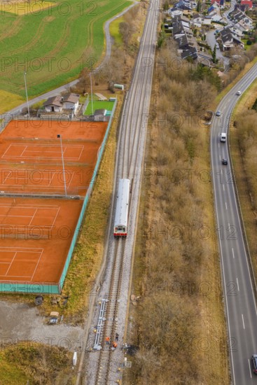 A train travels along railroad tracks past tennis courts, next to a busy road, historic event, first test run with a passenger train on the Hermann tracks, Hesse Railway since 1988, Calw district, Germany