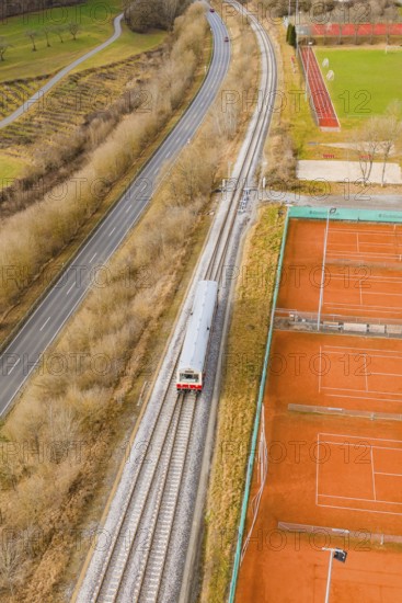 Railway tracks run next to tennis courts and a path in a wintry landscape, historic event, first test run with a passenger train on the Hermann tracks, Hesse Railway since 1988, Ostelsheim, Calw district, Germany