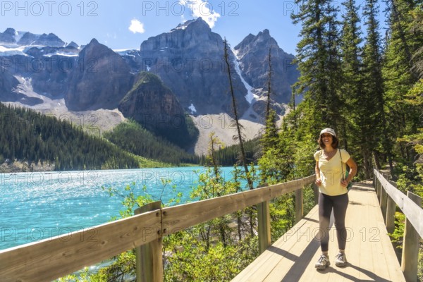 Female tourist walking along a wooden path, admiring the stunning turquoise waters of moraine lake and the majestic ten peaks in banff national park, alberta