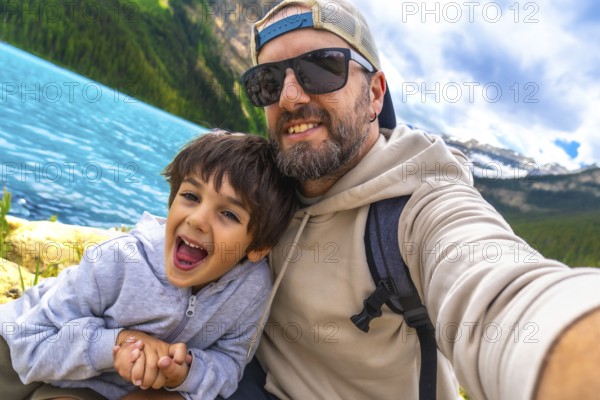 Happy father and son capturing a selfie by the turquoise waters of lake louise, surrounded by stunning mountains in banff national park, enjoying a memorable vacation