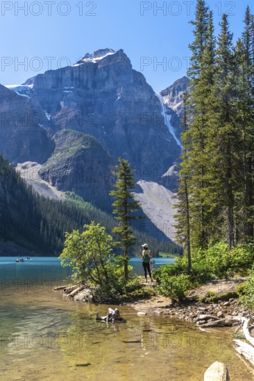 Female tourist walking along the scenic shores of turquoise moraine lake and enjoying the breathtaking view of the canadian rockies in banff national park on a sunny summer day