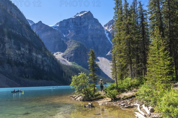 Tourists are canoeing on the turquoise, glacier fed moraine lake with its surrounding mountains and lush vegetation in banff national park, alberta, canada, during a sunny day