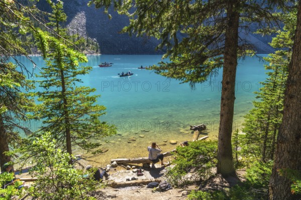 Tourists canoeing on the turquoise waters of moraine lake, surrounded by rocky mountains and lush pine forests in banff national park on a sunny summer day