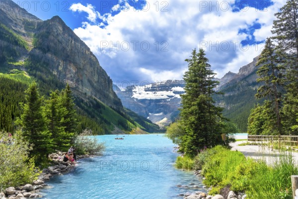 Turquoise water flowing into the stunning lake louise in banff national park, with tourists canoeing and enjoying the breathtaking landscape of mountains and lush vegetation