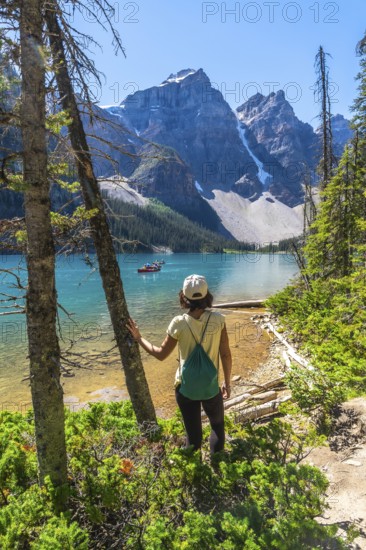 Female tourist admiring the turquoise waters of moraine lake with the valley of the ten peaks in the background, banff national park, alberta, canada, during a sunny summer day