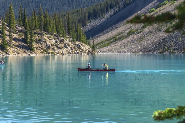 Two tourists paddling a red canoe on the turquoise waters of moraine lake in banff national park, surrounded by the breathtaking canadian rockies and lush pine trees