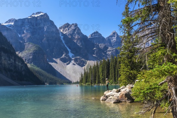 Moraine lake in banff national park displays its turquoise waters, surrounded by majestic mountains and lush vegetation, while a tourist admires the breathtaking landscape