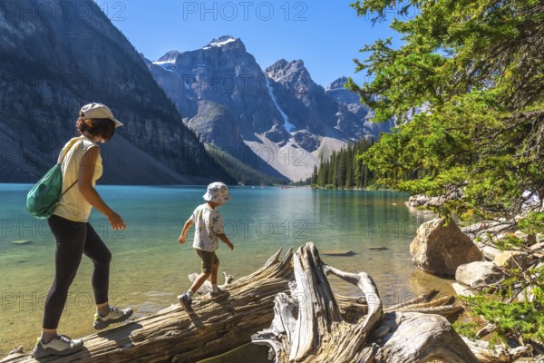 Mother and son enjoying a leisurely walk on a weathered log along the scenic shores of moraine lake, surrounded by the stunning canadian rockies on a sunny day