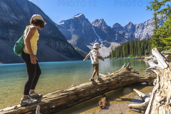 Mother and son balancing on a weathered log over turquoise waters of moraine lake, surrounded by the stunning canadian rockies in banff national park, enjoying a family adventure