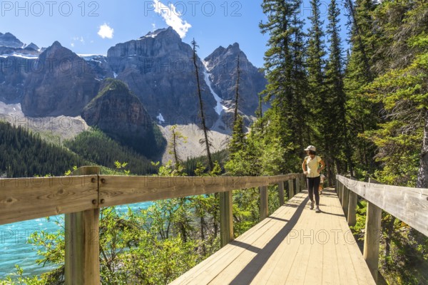 Female tourist walking on the rockpile trail admiring the turquoise color and the majestic mountains surrounding moraine lake in banff national park, canadian rockies, alberta, canada