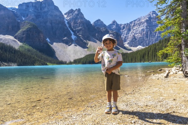 Young boy waving on the shore of moraine lake with the canadian rockies in the background, enjoying a sunny day in banff national park, alberta, canada, during summer vacation