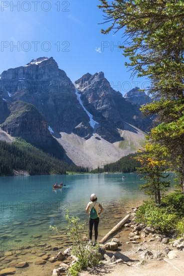 Female tourist standing on the shore of pristine turquoise moraine lake, admiring the majestic canadian rockies in banff national park on a clear summer day