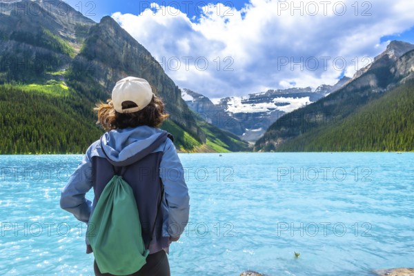 Female tourist admiring stunning turquoise waters of lake louise, framed by victoria glacier and the majestic canadian rockies in banff national park on a sunny summer day