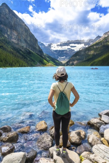 Young woman backpacker standing on rocks admiring stunning turquoise lake and surrounding mountains in banff national park, a popular tourist destination in the canadian rockies