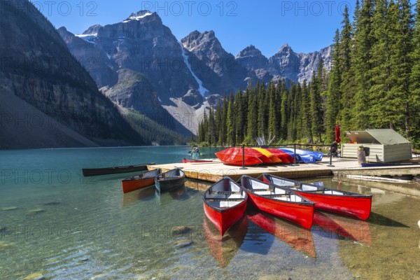 Reflecting red canoes in the turquoise waters of moraine lake, framed by snow capped mountains and pine trees, create a stunning landscape in banff national park, alberta