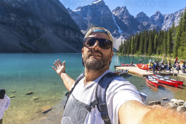 Backpacker taking a selfie with turquoise lake and canoes with the canadian rockies in the background at moraine lake in banff national park, alberta, canada