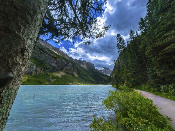 Sun shining through clouds illuminating turquoise waters of moraine lake and surrounding lush vegetation and mountains at banff national park in the canadian rockies, alberta, canada