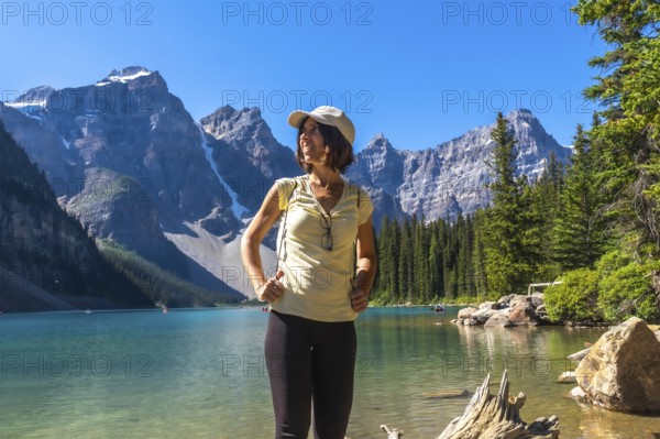 Female tourist standing at the shore of turquoise moraine lake enjoying the breathtaking view of the canadian rockies on a sunny summer day in banff national park, alberta, canada
