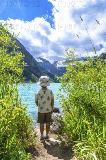 Young tourist admiring the stunning turquoise waters of lake louise, framed by victoria glacier and lush vegetation in banff national park during summer