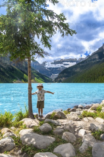 Young tourist with arms outstretched, enjoying the stunning turquoise waters of lake louise and the majestic canadian rockies in banff national park on a summer day