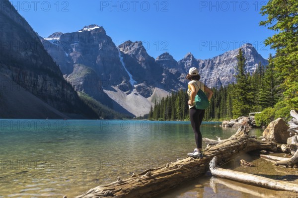 Female hiker standing on a log, admiring the stunning turquoise waters of moraine lake and the majestic mountains in banff national park on a sunny summer day