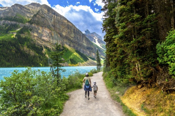 Mother and son walking along the scenic turquoise waters of lake louise with surrounding mountain peaks and lush green forest in banff national park, canadian rockies, alberta, canada