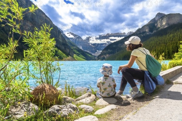 Mother and her child are sitting on the rocky shore of the turquoise lake louise, enjoying the breathtaking view of the canadian rockies in banff national park, alberta, on a sunny day