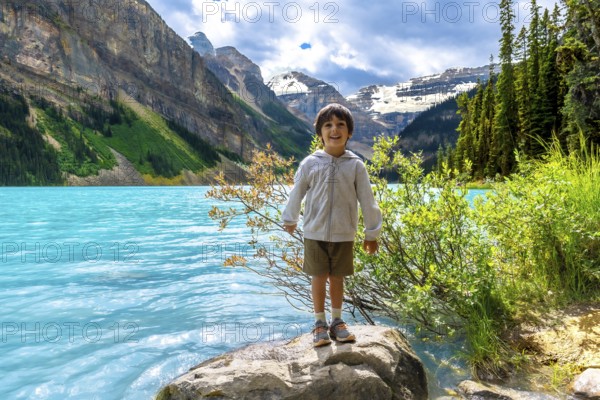 Happy child standing on a rock by the turquoise water of lake louise, enjoying the stunning scenery of the canadian rockies in banff national park, alberta, canada, on a beautiful summer day