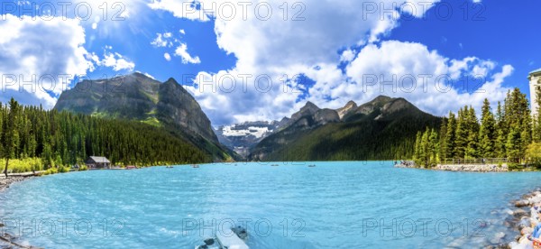 Panoramic view of tourists canoeing on turquoise lake louise, featuring the iconic fairmont chateau hotel amid mountains and pine trees in banff national park