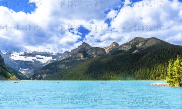 Canoeing on the turquoise waters of lake louise, tourists enjoy a breathtaking summer landscape framed by snow capped mountains and lush green forests in banff national park