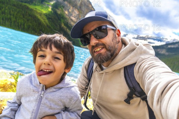 Father and son capturing a selfie by the turquoise waters of lake louise, surrounded by stunning mountain views during a memorable vacation in banff national park