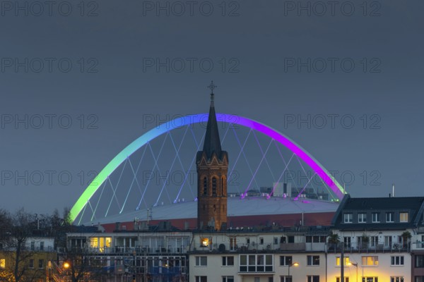 Evening view of residential buildings on the banks of the Rhine, behind them the church tower of St. John's Church and the rainbow illuminated arch of the Lanxess Arena, Cologne-Deutz, Cologne, North Rhine-Westphalia, Germany