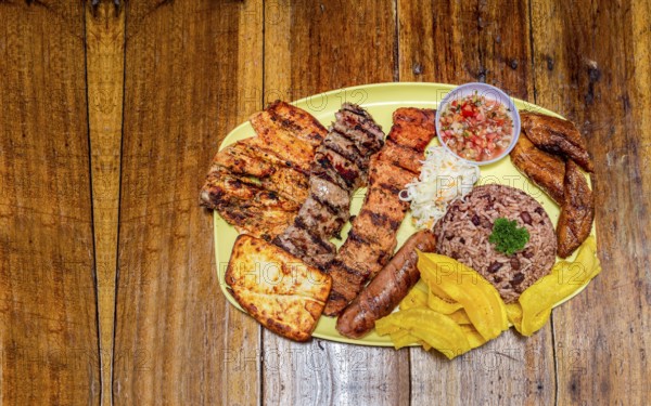 Varieties of grilled meats with rice, fried cheese and tomato salad, plate with assorted types of grilled meats on wooden table, traditional Nicaraguan food served on wooden table