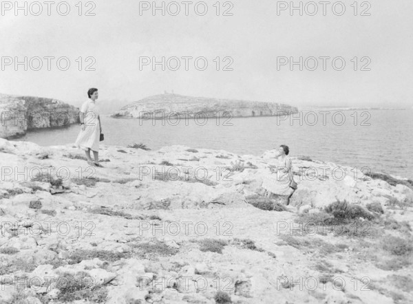 Two young woman at rocky coastal area with St Paul's Island in background, St Paul's Bay, Malta, Europe, 1956