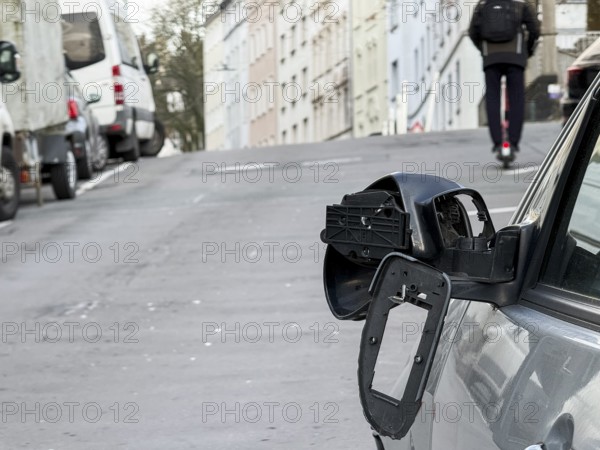 A car on the side of a steep residential street. The vehicle's left wing mirror is severely damaged and part of the mirror is on the hood, Wuppertal, Germany