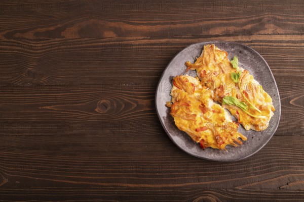 Baked chicken meat with cheese and tomatoes on brown wooden background. top view, flat lay, copy space