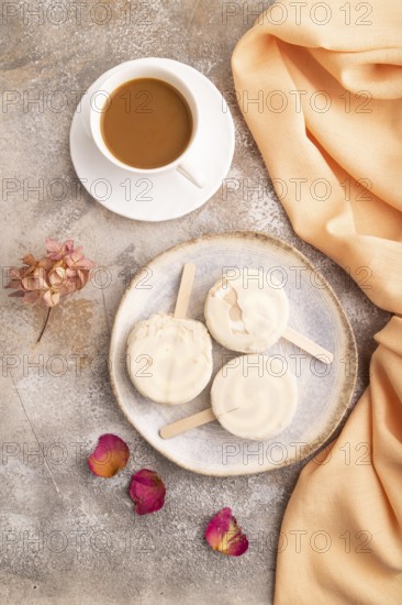 ?hocolate Ice cream in white glaze, cup of coffee, on brown concrete background and orange textile, top view, flat lay, close up, minimalism