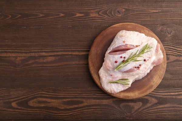 Raw Turkey Thigh with spices and rosemary on cutting board on brown wooden background. top view, flat lay, copy space