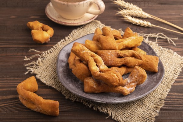Crunchy biscuit Brushwood cookies sprinkled with powdered sugar on brown wooden background and linen textile, cup of coffee, side view, close up