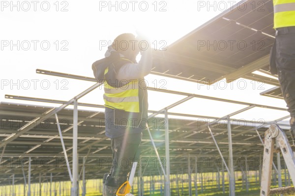 Person mounts solar panel on frame, bright sun in background, Energiewende, construction of PV open space, Baden-Württemberg, Germany