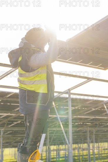 Man installing solar panel, wearing safety vest, with sun rays in the background, Energiewende, construction of PV open space, Baden-Württemberg, Germany