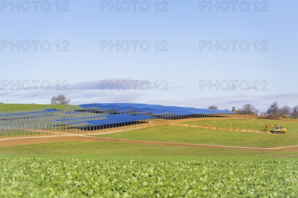 A tractor works in a field with installed solar panels under a blue sky, Energiewende, construction of PV open space, Baden-Württemberg, Germany