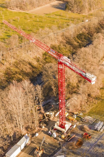 Red crane on a construction site, surrounded by autumnal forests and seen from the air, construction of the Hermann Hesse Railway, Calw, Germany
