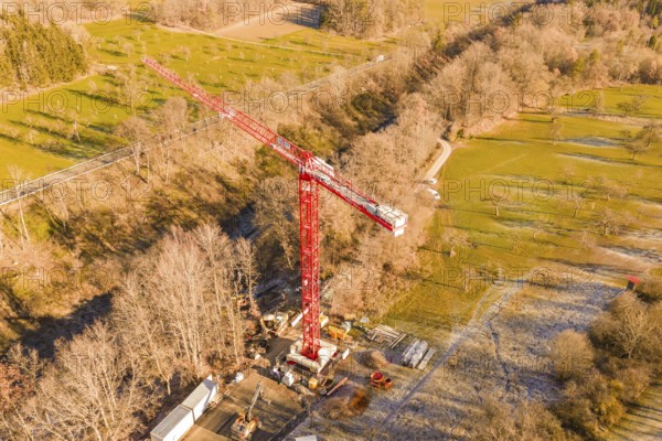 Red crane on construction site in autumn landscape with forests and meadows from a bird's eye view, construction of the Hermann Hesse Railway, Calw, Germany