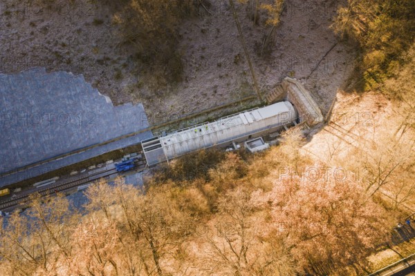 A train emerges from a tunnel located in a forested and frosty environment, construction of the Hermann Hesse Railway, Calw, Germany