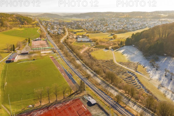 A railway traverses a scenic winter landscape with fields and a nearby village, construction of the Hermann Hesse Railway, Calw, Germany