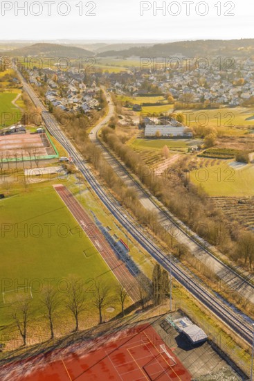 A railway line runs alongside fields and a sports complex near a village in winter, construction of the Hermann Hesse Railway, Calw, Germany