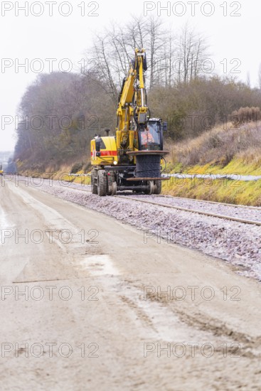 A yellow excavator works on a construction site along the tracks on a road, building the Hermann Hesse Railway, Calw, Germany
