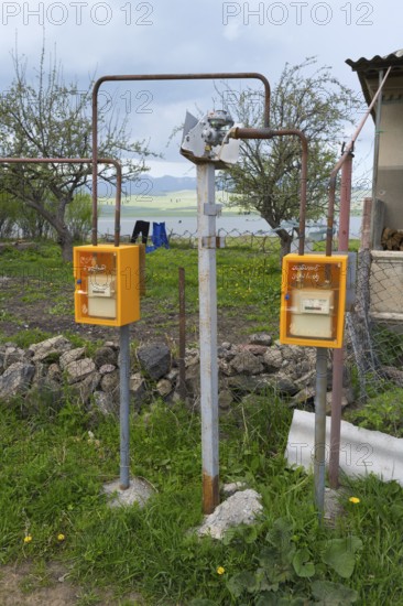 Two yellow gas meters stand on the side of a rural building with trees in the background, Sameba, Kvemo Kartli region, Lower Kartli, Georgia