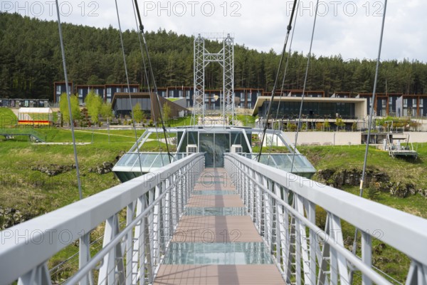 View of a modern suspension bridge with buildings in the background and surrounded by forest, Diamond Bridge, Diamond Glass Bridge, world's longest free-hanging structure, Dashbashi Gorge, Khrami River, Chrami, Tsalka Nature Reserve, Kartli, Georgia